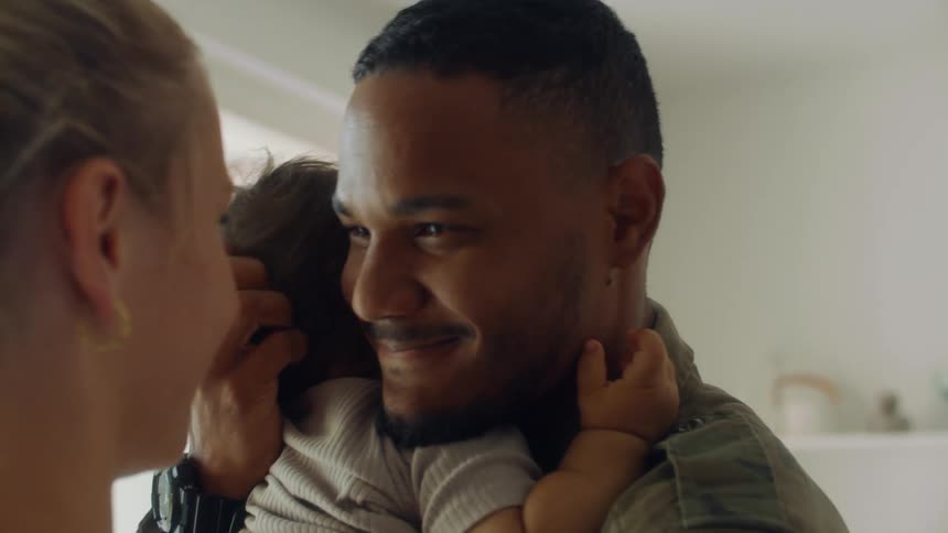 A father and mother kissing while holding their baby