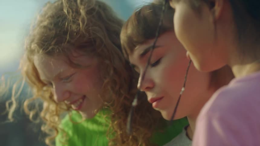 A group of young women talk and laugh together while standing outside