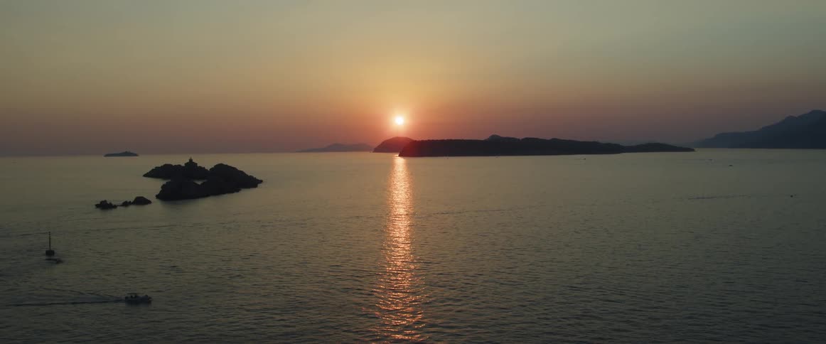 A sunset emits a beam of red tinted light onto the sea below