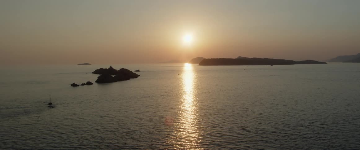 A body of water with islands with the sun the sky and clouds in the background