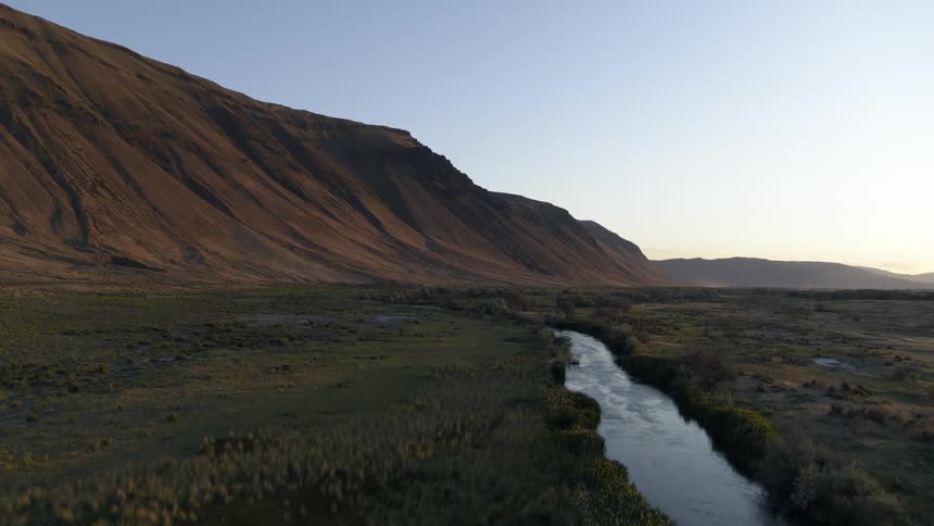 The sunset sky reflects on the surface of a winding stream along a beautifully contoured mountainside