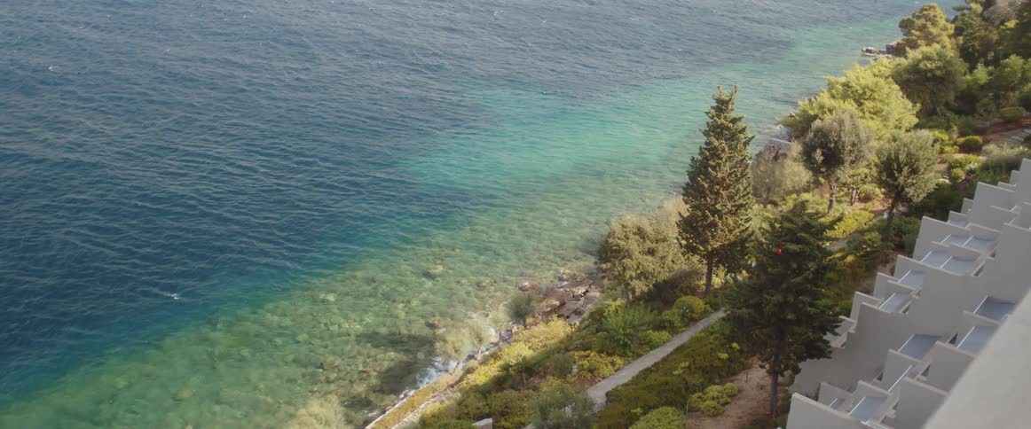 The view looking over the edge of a balcony is a high cliff overlooking a coastal area on the ocean