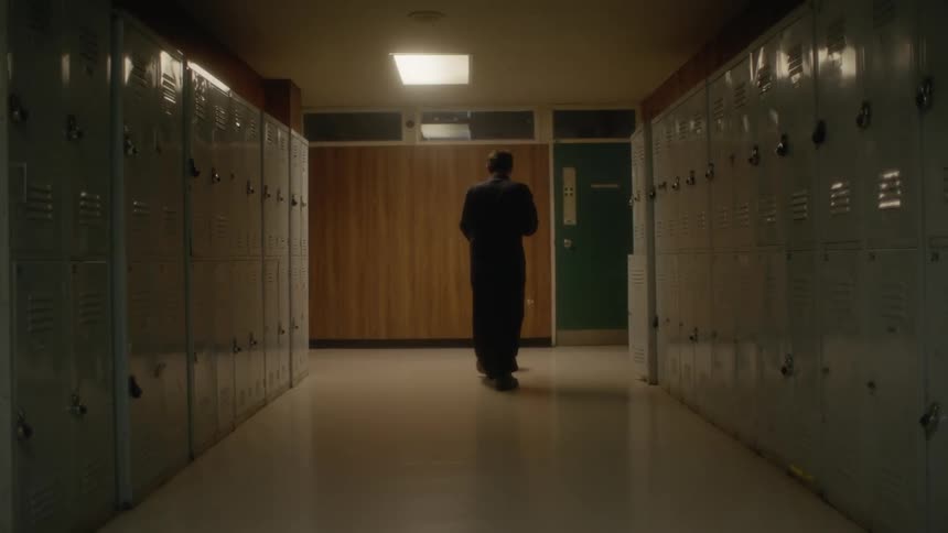 A janitor pushing a mop and bucket down an empty school hallway at night