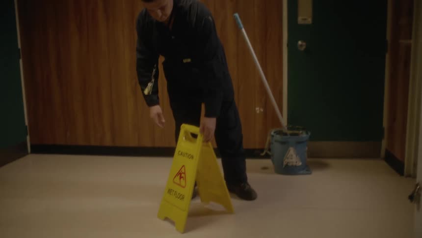 A janitor places a wet floor caution sign in a locker room
