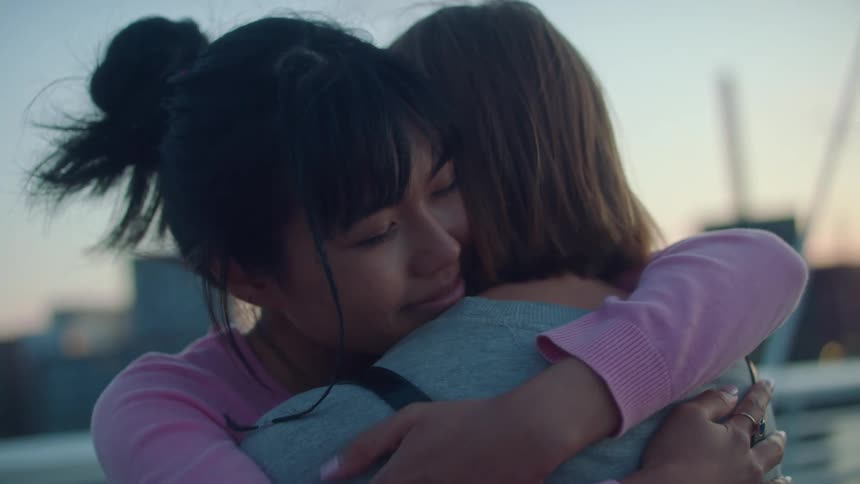 The woman leans forward to give her friend a caring hug and gently rubs her back
