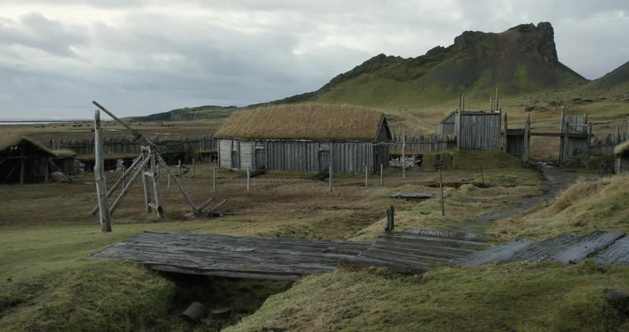 Small wooden huts sit on a grass field on an abandoned viking village