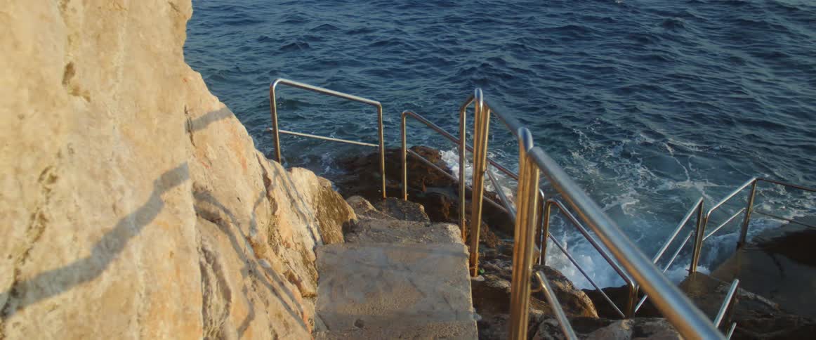 Railings line stone steps leading down to ocean waves splashing against the rocks