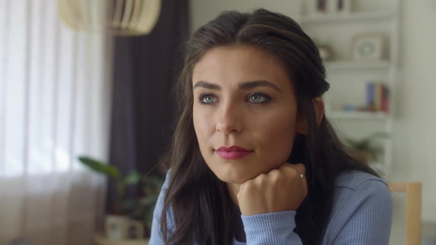 A woman is sitting at a table with her chin resting on her hand