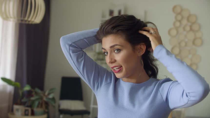 A woman with long brown curly hair runs her fingers through it while talking to somebody else as if shes giving a tutorial