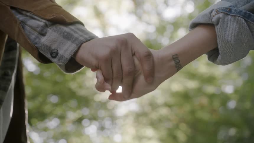 Two people hold hands with the sun shining in the background
