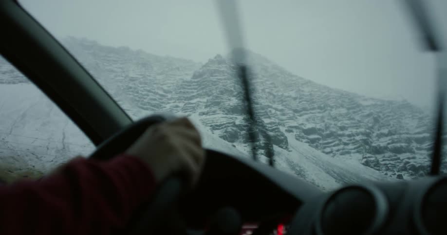 A car is driving near a mountain covered with snow