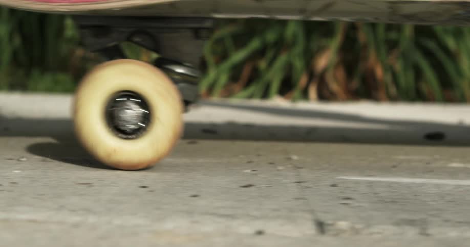 The wheels of a skateboard are seen rolling down a sidewalk