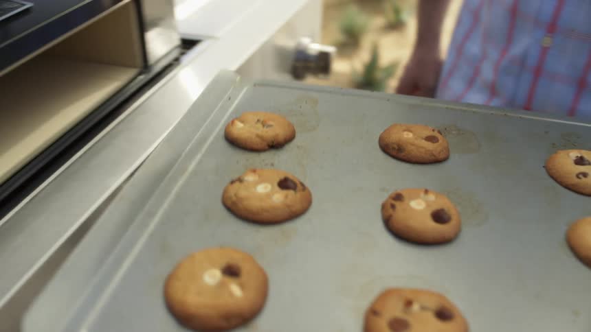 A man uses an ovenmitt and takes a pan of cookies out of an oven