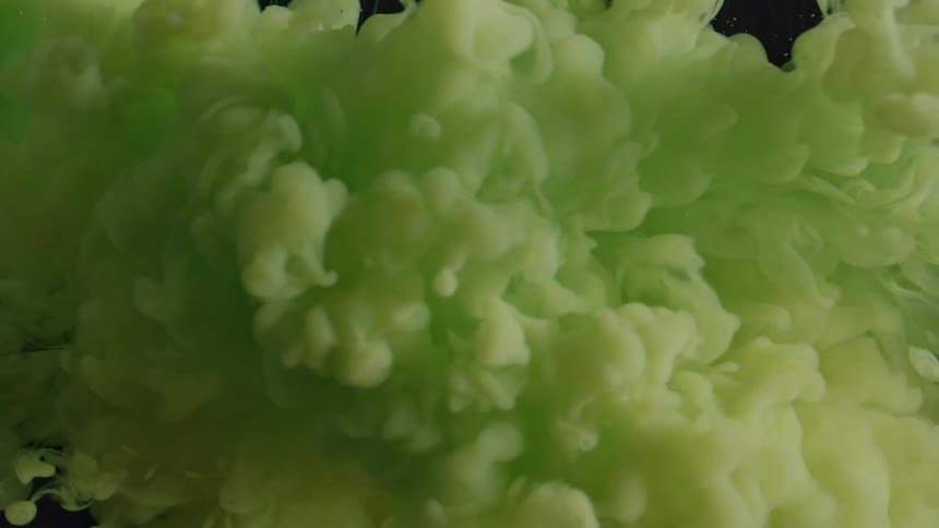 Clouds of bright green liquid ink mixing inside a water tank over a black background