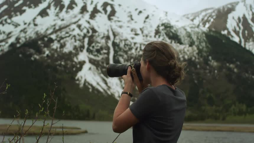 Female photographer takes photos of lake and high snowy mountains