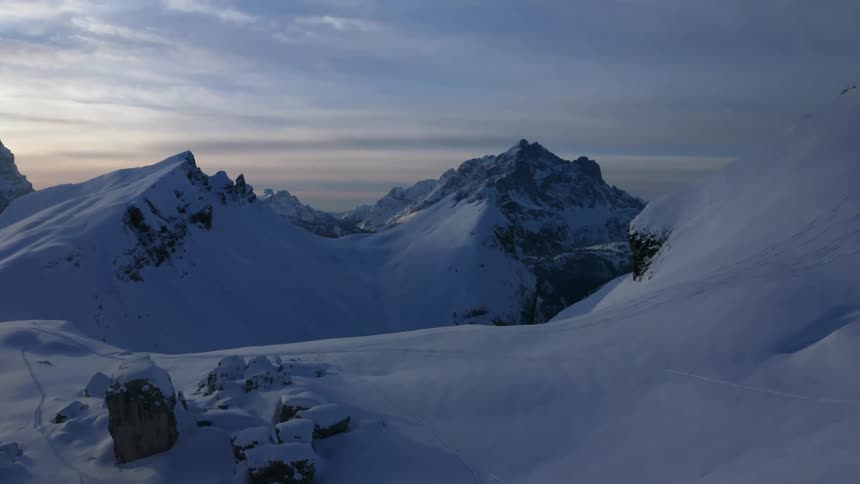 Snow covered mountains with peaks high in a cloudy sky as the sun is setting