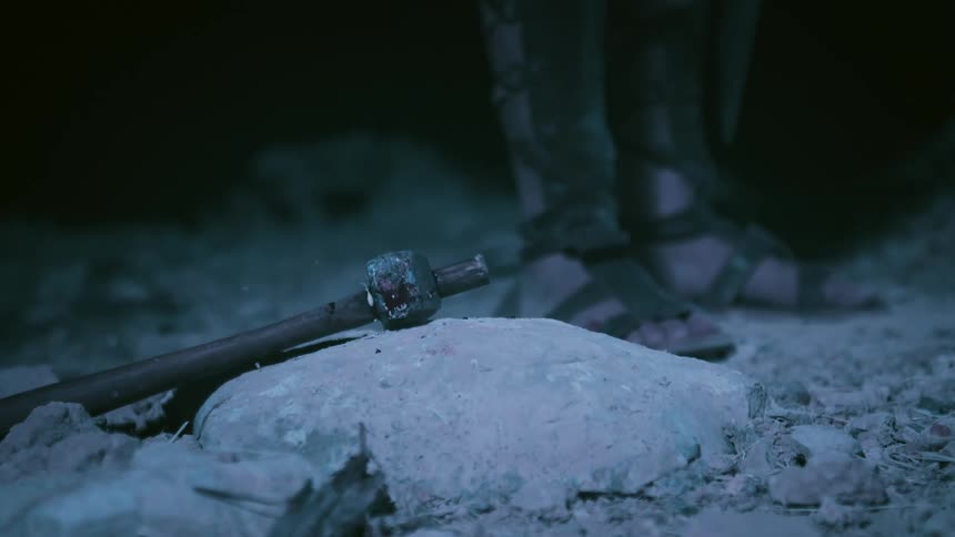 Hammer falling over a rock on the ground neara man wearing sandals at night