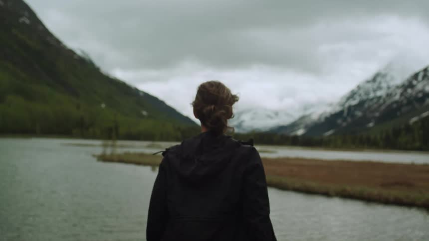 Woman standing on the coast of a lake in the mountains under the clouds