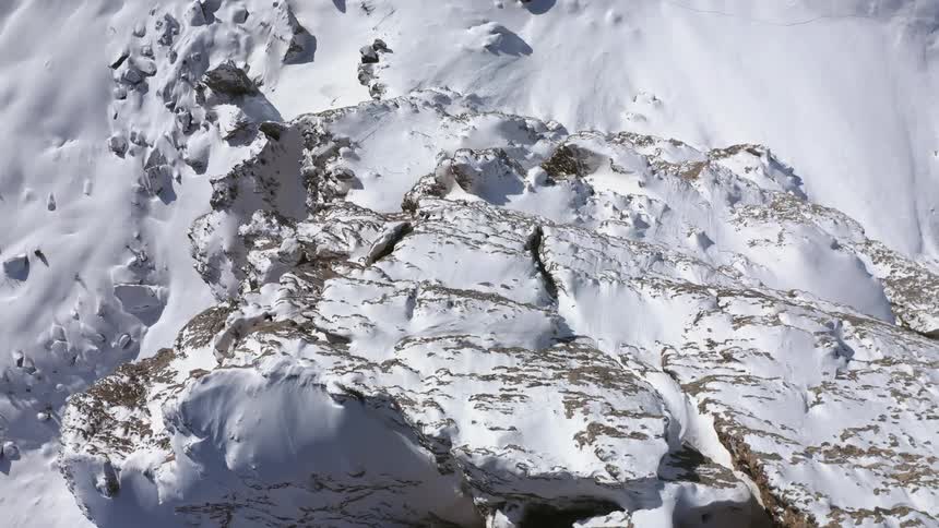 The camera captures an aerial view of the top of a mountain peak that is completely covered in snow