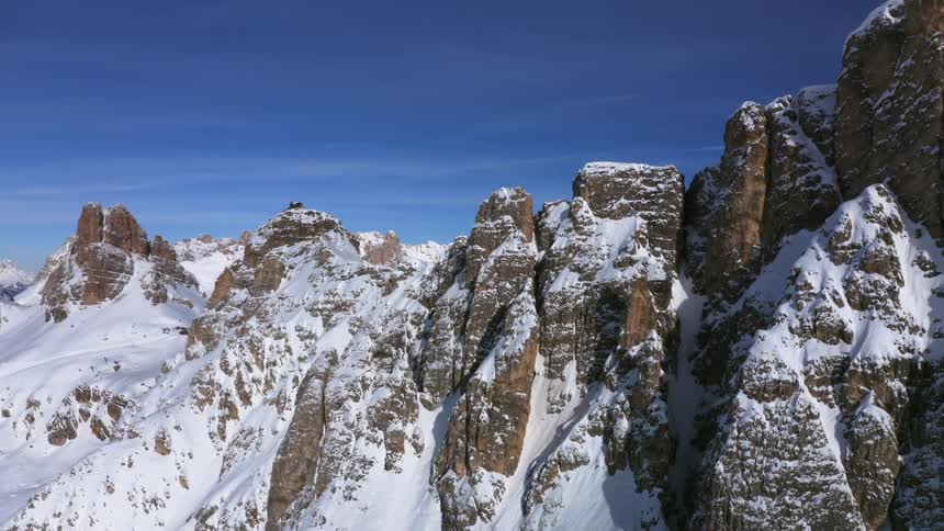 A range of rocky mountains are completely covered in snow under a clear blue sky