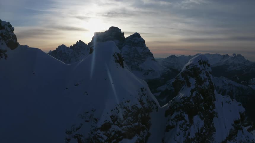 Snow covered mountains with peaks high in a cloudy sky as the sun sets