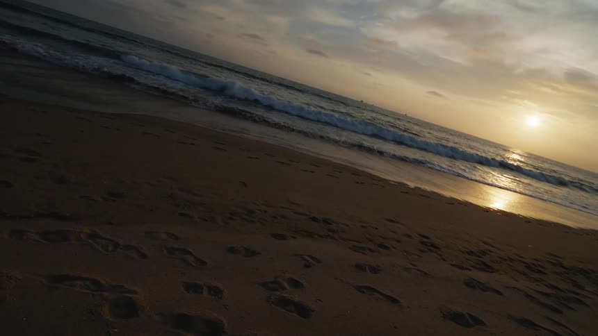 A shot of waves coming at the shore of a beach with sun visible in the background