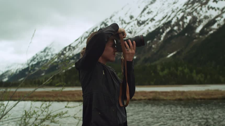 Young woman takes pictures of a lake in the mountains with a camera