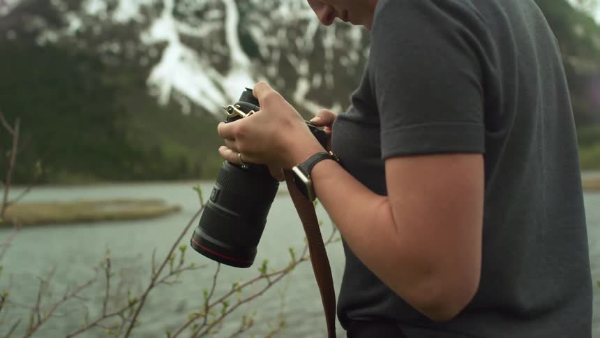 A woman is standing at the waters edge as she looks into her camera