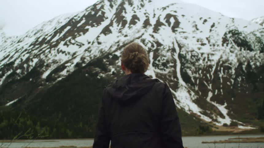 Young woman walking near the coast of a lake on the snow covered mountains