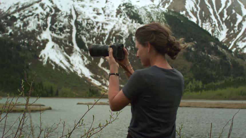 Young woman takes pictures of a lake in the mountains with a camera
