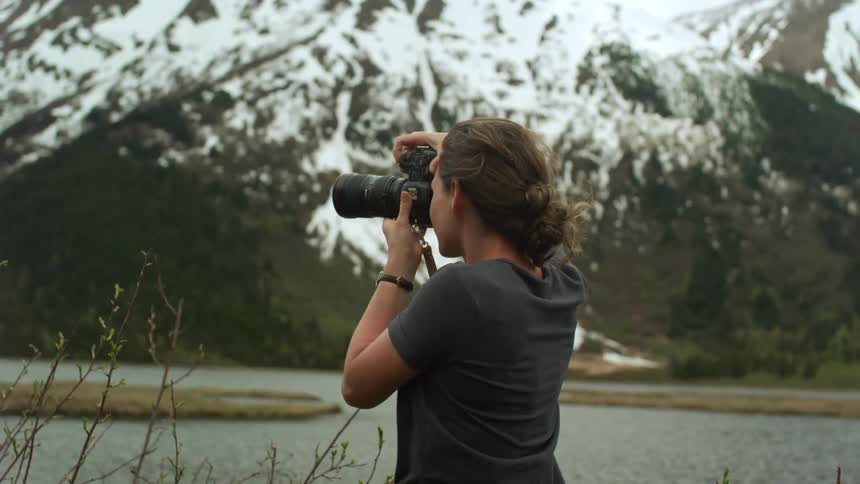 Young woman taking pictures of a lake near the mountain with a camera