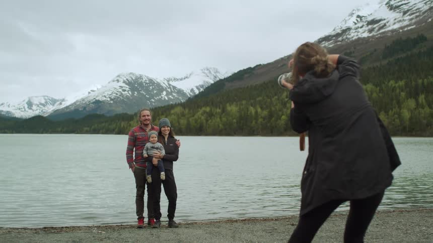 Photographer takes pictures of a family standing on the coast of a lake in the mountains