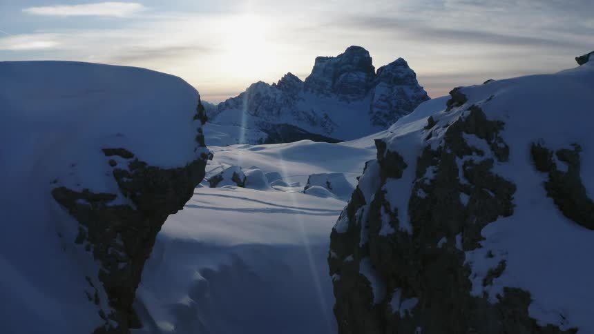 Snow covered mountains and peaks high in a cloudy sky as the sun goes down