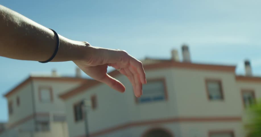Woman holds hand outside moving vehicle passing by apartment buildings under blue sky on sunny day