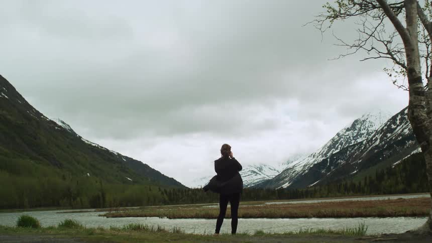Woman uses a camera to take pictures of a lake near the mountains