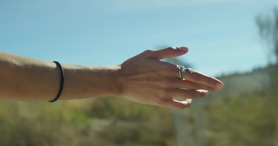 Woman holds arm outside traveling vehicle during road trip passing hills and road signs