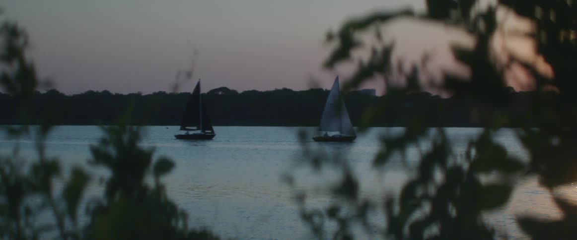 Two boats sail across the lake at sunset