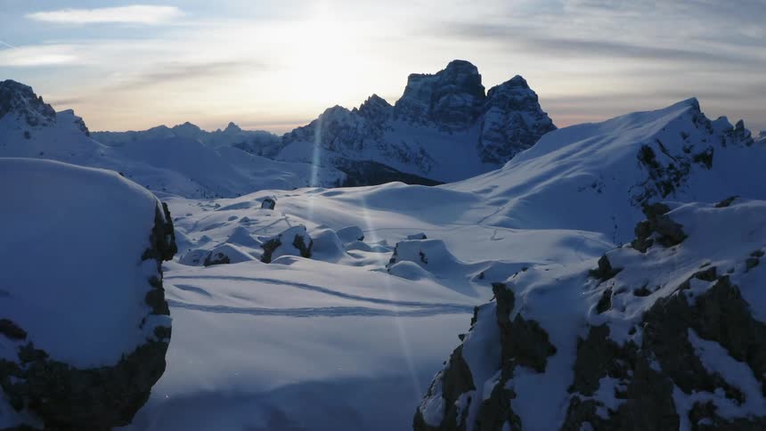 Snow covered mountains with peaks high in a cloudy sky as the sun is setting