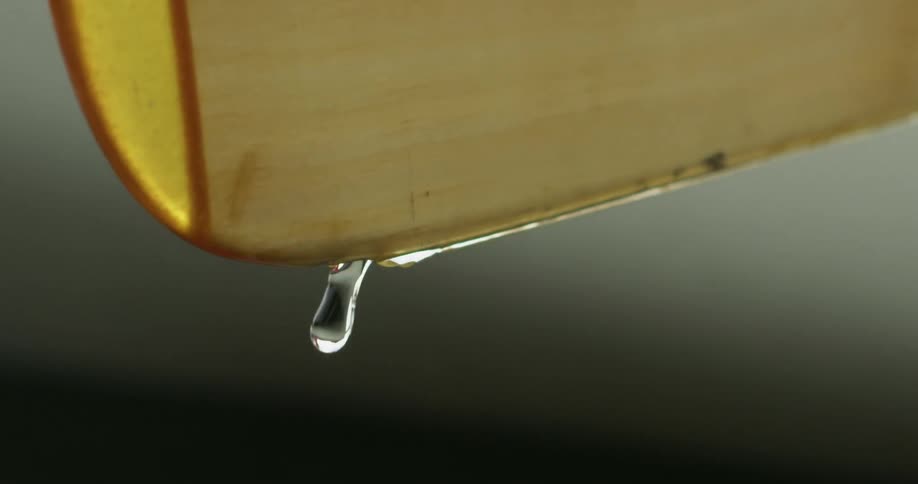 A close daytime view of water dripping from a pitcher as the water is being poured