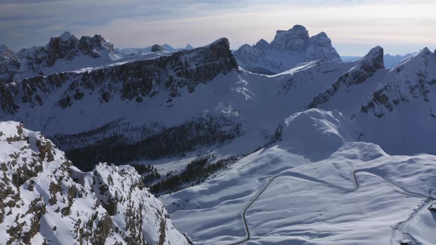 Aerial view of snowy high mountain peak looking over valley with forest