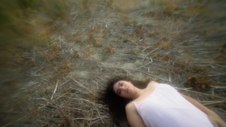 A woman wearing a white nightgown lying on the ground turns her head
