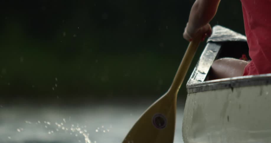 Woman rowing a boat using an oar on a lake under the rain