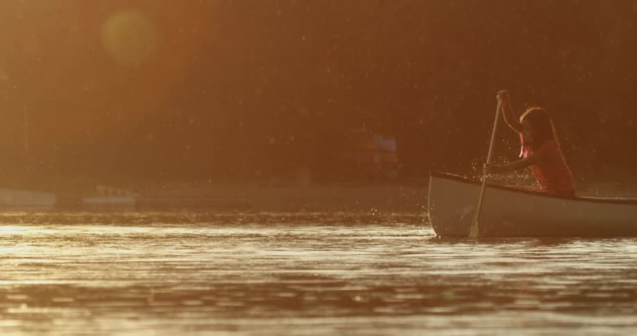 A woman is paddling a boat in a water body