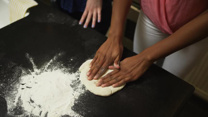 A woman flattening dough on a table with cooking flour