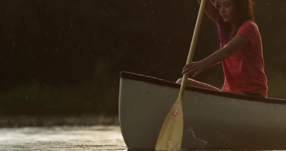 A woman wearing an orange tshirt is rowing a canoe