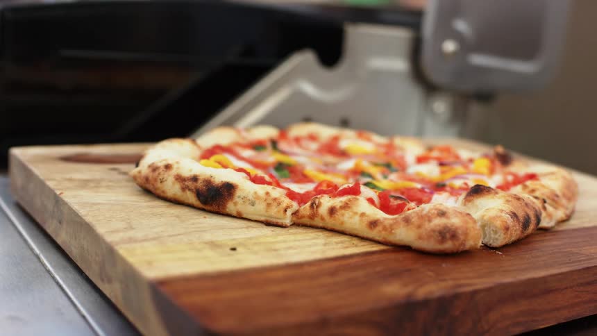 Man uses a sharp knife to cut slices of pizza over a wooden board