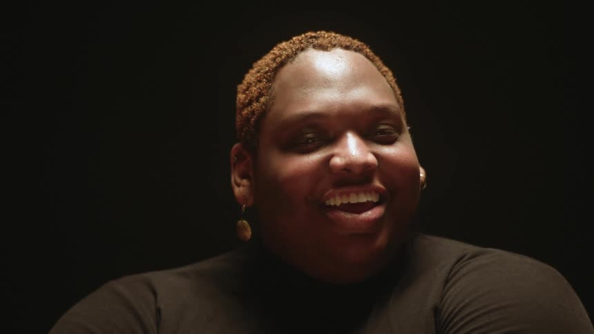 Male dancer with short brown hair and earrings looks at the camera laughing
