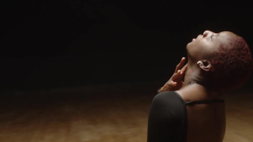 A woman in a leotard dances with great emotion in a studio with a hardwood floor
