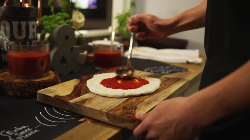 Man serving and spreading tomato sauce over pizza doug at home