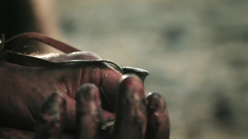 A metal hammer drives a metal spike that is placed above a persons wrist and hand